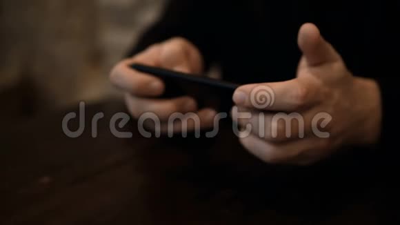 近距离观看男性手握智能手机时坐在咖啡馆的桌子浏览互联网视频的预览图