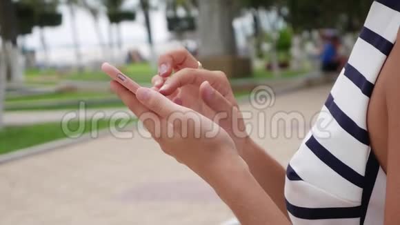 一位年轻漂亮的苗条女士身穿黑白连衣裙留着金色长发坐在长凳上使用智能手机视频的预览图
