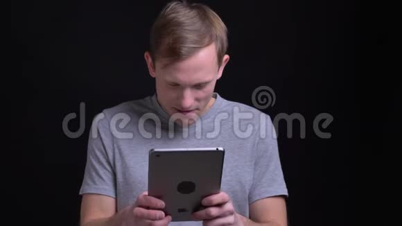 年轻英俊的白种人在镜头前的平板电脑上打字的特写肖像背景被隔离视频的预览图