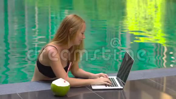 快乐微笑的女性自由职业者坐在热带游泳池里的笔记本电脑上视频的预览图
