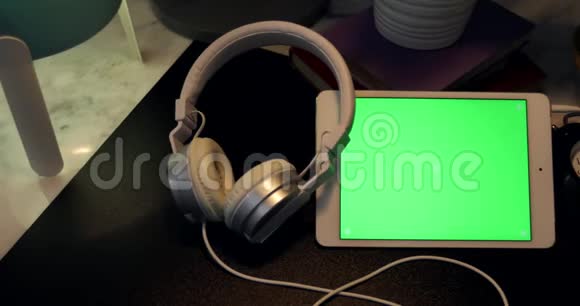 数码平板电脑上的绿色屏幕和晚上书桌上的耳机的多利拍摄视频的预览图