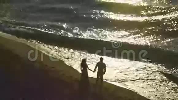 夕阳西下海岸迷人的一对剪影一对夫妇看起来像海浪在沙质海岸线上视频的预览图