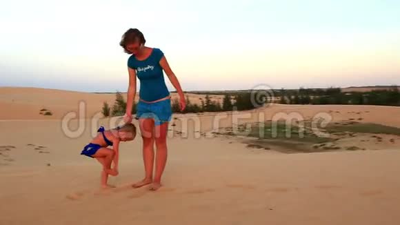 母亲小女孩摇沙从腿上的沙丘在黄昏视频的预览图