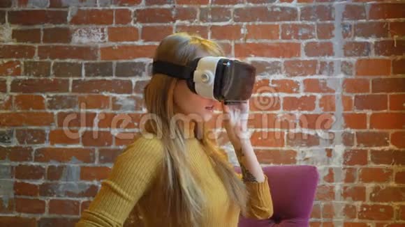 有魅力的年轻女性戴着VR耳机坐在家中打手势微笑视频的预览图
