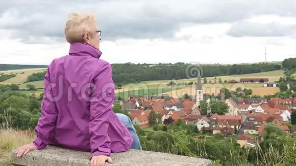 一位年长的妇女坐在长凳上望着小镇视频的预览图
