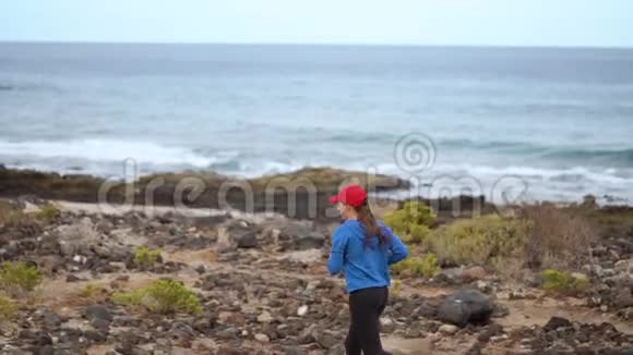 女人沿着海洋的石岸奔跑健康的积极生活方式慢动作视频的预览图