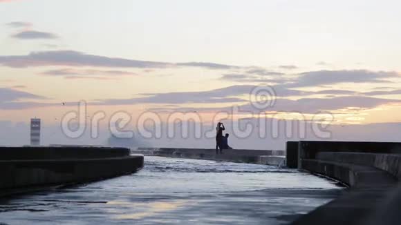 年轻夫妇在有灯塔的防波堤码头享受日落视频的预览图
