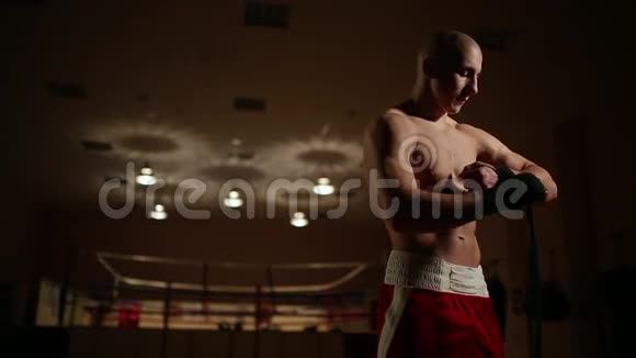 一个穿着拳击靴和短裤的男人在健身房里打着拳击戒指的背景他的身上绑着绷带视频的预览图