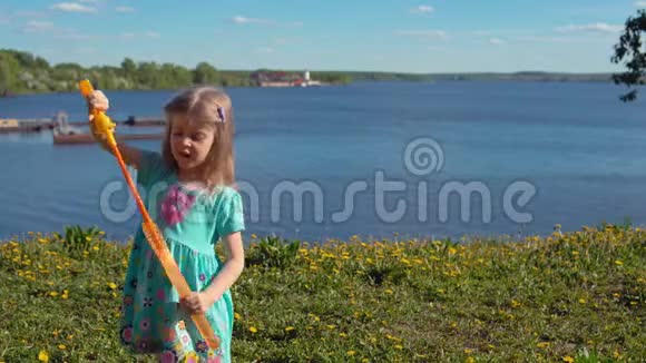 在海岸的背景下金发小女孩膨胀了巨大的肥皂泡视频的预览图