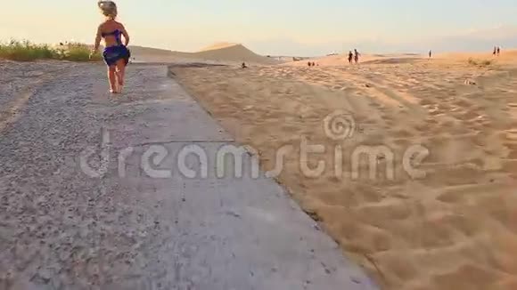 日落时分小女孩赤着脚沿着沙丘的小径奔跑视频的预览图