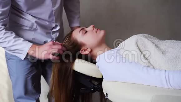 按摩治疗师为白天躺在医生办公室沙发上的女客户做头部按摩视频的预览图