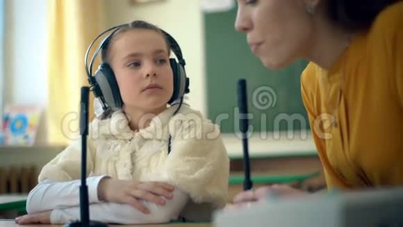 在教室里使用耳机和麦克风的年轻女孩和老师视频的预览图