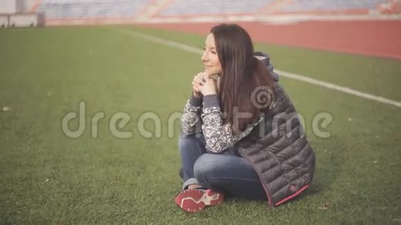 足球场上美丽的年轻女子女孩坐在操场上的绿草上视频的预览图