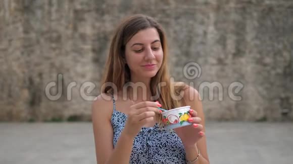 街头卖杯冰淇淋的可爱年轻女人用勺子吃饭视频的预览图