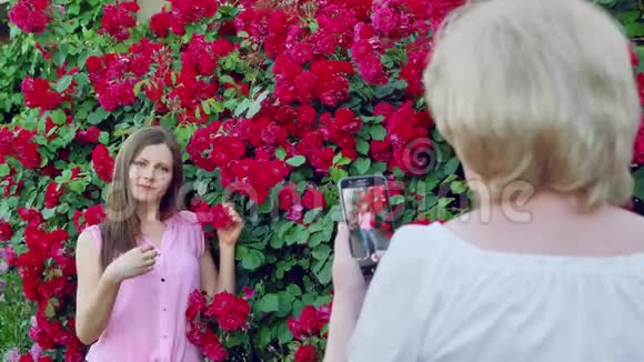 年长的女人拍照年轻的女孩妈妈给女儿拍照红玫瑰花在背景上视频的预览图