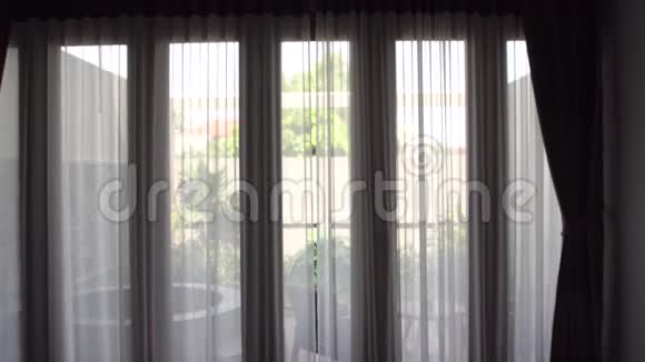 穿着浴袍的女人拉开窗帘看着站在窗边的花园视频的预览图