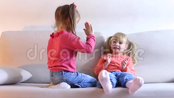 两个漂亮的小女孩在沙发上玩耍和玩耍视频的预览图
