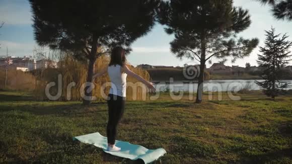 年轻迷人的女孩在公园里做运动躺在瑜伽垫上伸展身体健康的积极观念视频的预览图