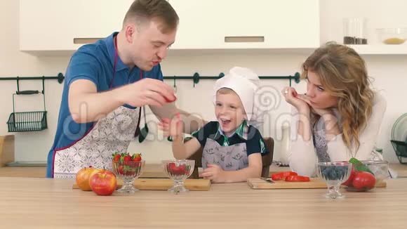 父母在厨房里用草莓喂儿子他们正在准备早餐视频的预览图