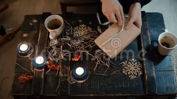 顶部特写女性手制作礼物坐在家里的桌子上女人用丝带绑一个圣诞盒子视频的预览图