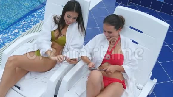 两个美女在泳池边用手机和平板电脑视频的预览图