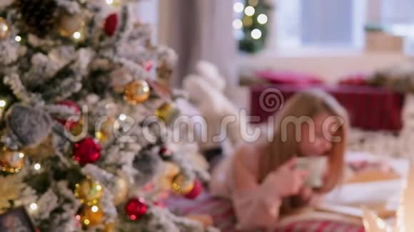 年轻的女人躺着一杯茶和一本书在圣诞节的内部躺在床上视频的预览图