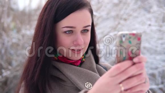 年轻漂亮的女孩穿着外套在冬天的公园里写着一条信息视频的预览图