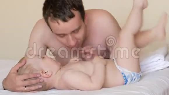 父亲亲吻他的小儿子挠他的痒痒他们睡觉后躺在床上婴儿不到两岁视频的预览图