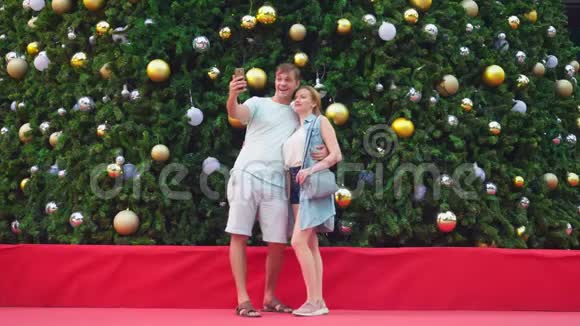 一对幸福的夫妻站在圣诞树的背景下在手机上自拍视频的预览图