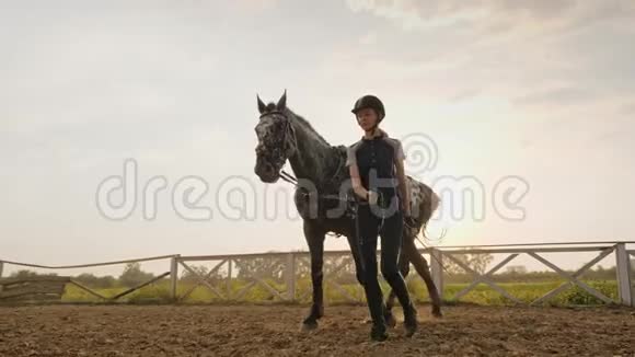 年轻的骑师女孩在美丽的夕阳下牵着她的马慢动作视频的预览图