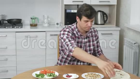 男人正在家里的餐桌上做饭皮塔蔬菜和葱配酱汁和蛋黄酱视频的预览图