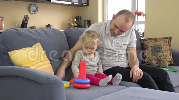 父亲带着孩子女儿在沙发上玩五颜六色的教育圈金字塔视频的预览图