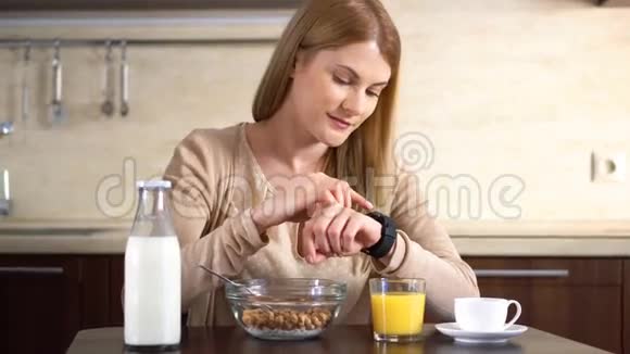 漂亮迷人的女人在吃早餐用她的智能手表浏览互联网在看新闻视频的预览图