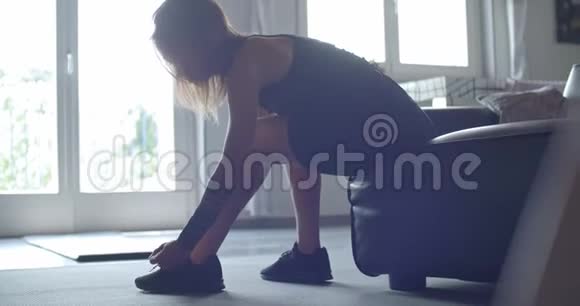 穿着纹身的运动女人在家健身前先系鞋带客厅家政培训4k慢动作视频的预览图
