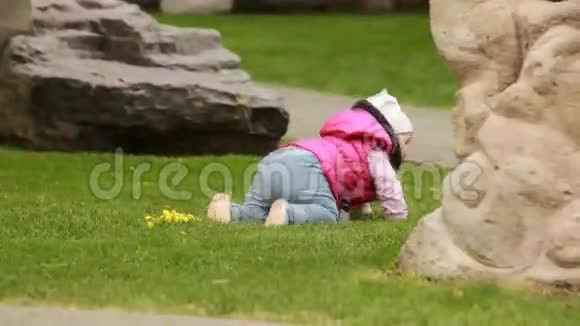 可爱的微笑女婴爬在城市公园的绿草上视频的预览图