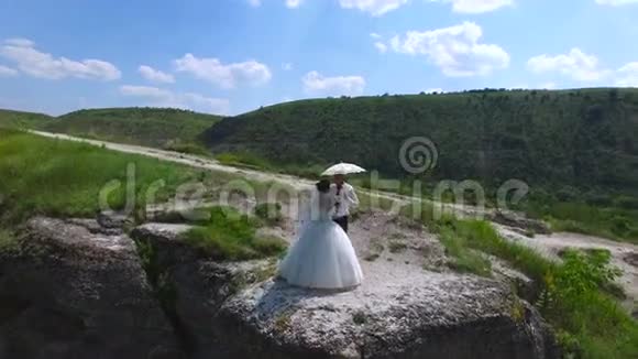 站在河边悬崖上的新婚夫妇的鸟瞰图视频的预览图