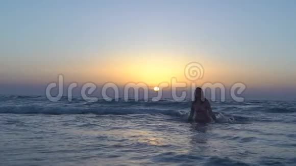 穿着粉红色泳衣的漂亮女人正在海滩上跑步晒太阳坐在海里或海洋里快乐的女孩奔向日落视频的预览图