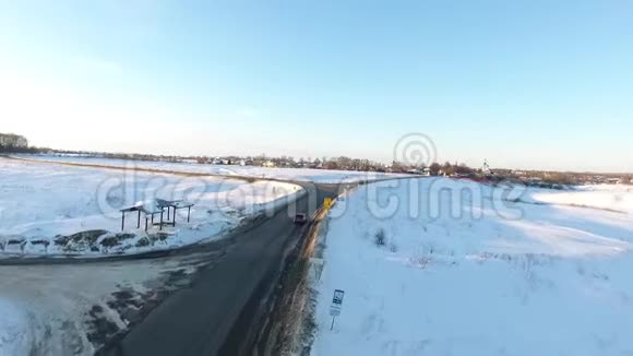 在金色日出时空中近距离飞行在汽车上方沿着雪道行驶在寒冷的道路上行驶的汽车视频的预览图