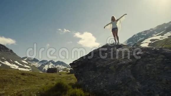 浪漫的女孩梦想着飞行而站在山上的岩石背景上的灿烂阳光视频的预览图