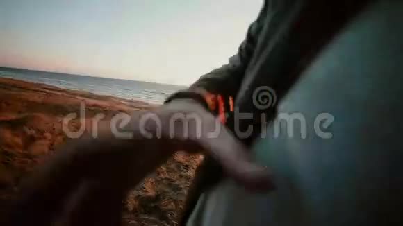 日落时分一个穿着棕色牛仔裤和深色皮夹克的高个子帅哥站在海滩上视频的预览图