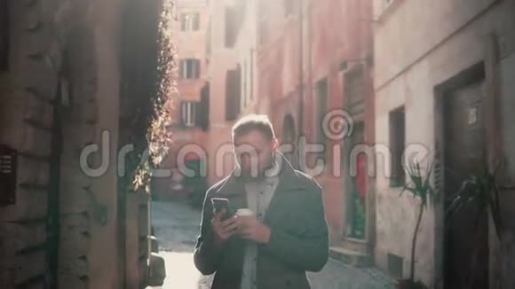 微笑的年轻人早上在城市里散步用智能手机家伙浏览互联网短信与某人视频的预览图