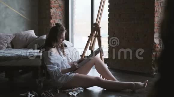 在工作的肖像艺术家女孩画了一幅坐在家里工作室地板上的画视频的预览图