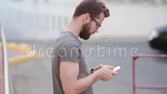 年轻时尚的商人站在街上使用智能手机戴着胡子戴着眼镜的人在和别人聊天视频的预览图