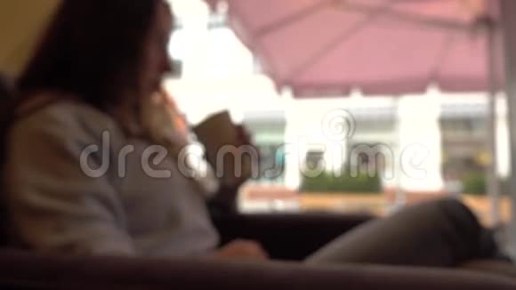 一个头发模糊的黑发女孩在窗边的一家咖啡馆里拿着吸管喝酒4K背景boke剪辑视频的预览图