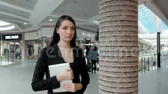 一位迷人的年轻女性站在相机前手里拿着平板电脑中镜头的商务女性在办公室散步视频的预览图