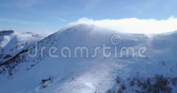 前方空中冬季雪山山顶滑雪道度假村与滑雪者滑雪晴天雾蒙蒙的云福克视频的预览图