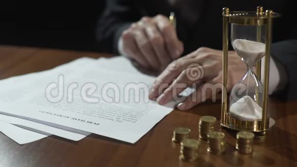 男性买方或卖方签署购买协议钱和沙漏在桌上视频的预览图