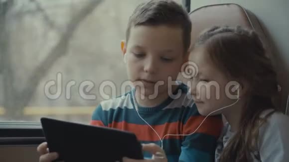 一个年轻的男孩和女孩乘公共汽车穿过城市在电脑平板上看电影的特写镜头视频的预览图