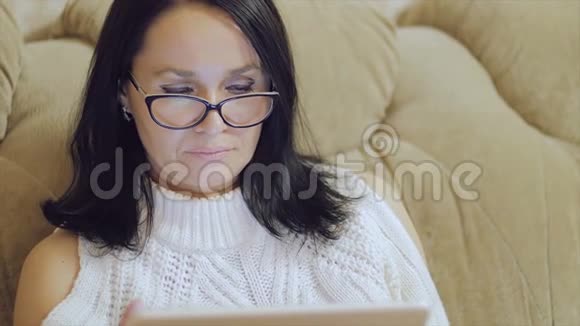 一个戴眼镜的女人坐在沙发上手里拿着一块平板电脑视频的预览图