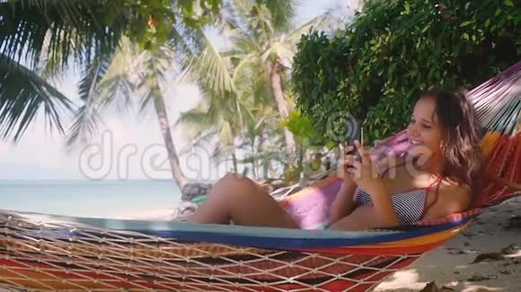 迷人的年轻快乐的女人使用移动电话在海滩附近的海滩和棕榈树泰国高清慢慢视频的预览图